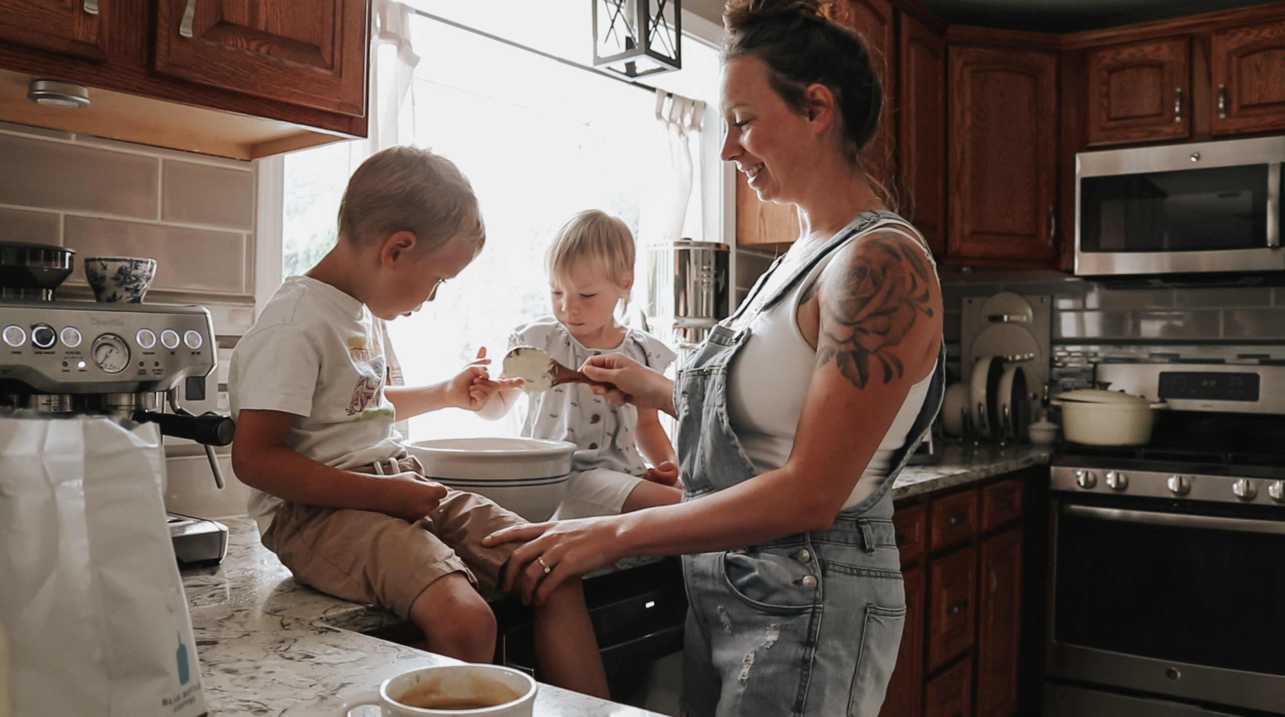 Christian Homemaker holds baby while her other children sit on the kitchen counter, they are eating together